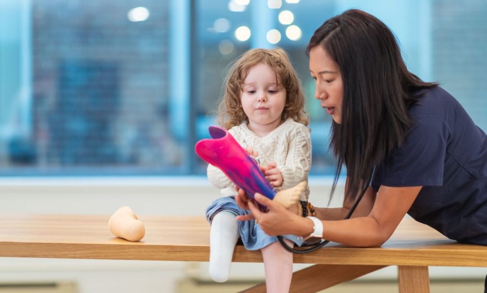 Toddler girl and an adult woman. Both are looking at a bright coloured prosthetic leg.