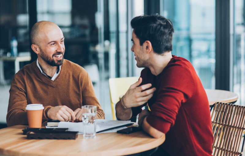 2 men smiling and having a chat at a round desk