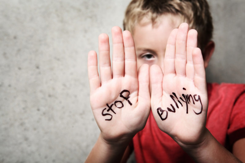 Child holding hands up with "stop bulling" written on palms in black texta